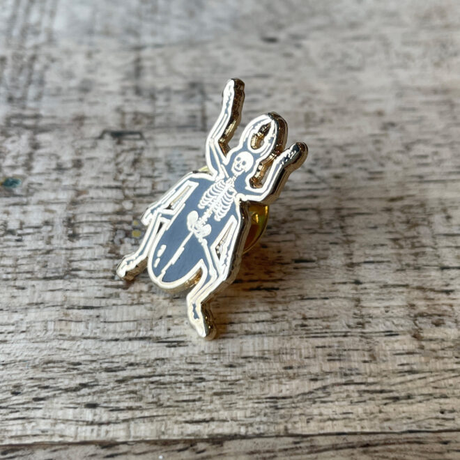 Metamorphosis - Enamel Pin Badge - Skeleton Beetle - against wood - image 2